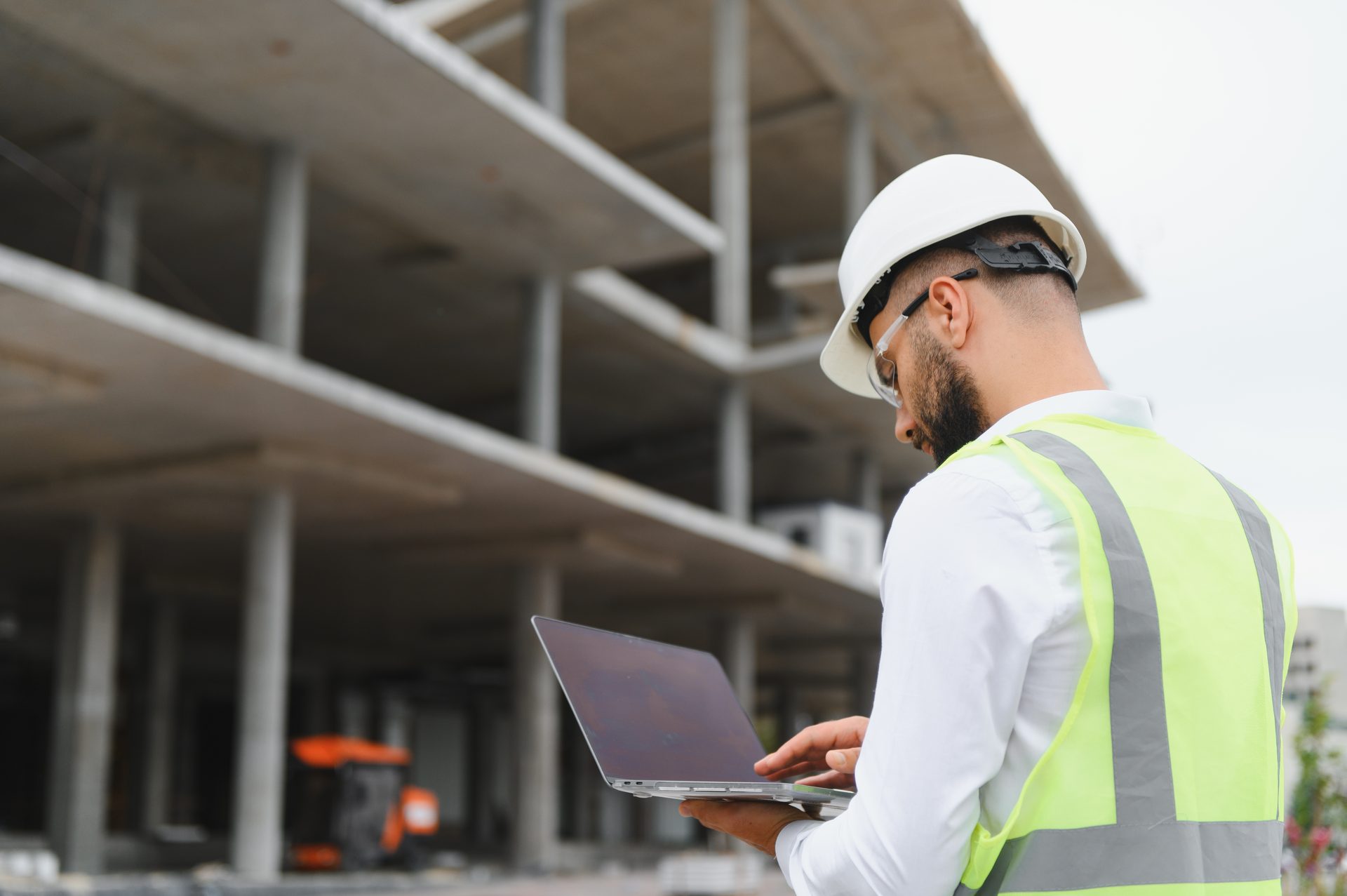 Bauleiter mit Laptop und Schutzausrüstung koordiniert die Arbeiten auf der Baustelle
