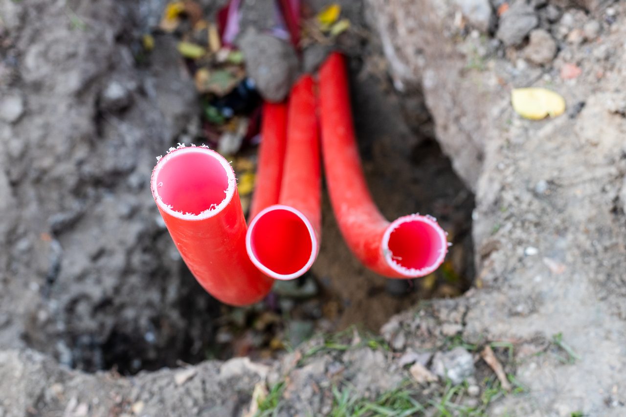 Rote Kabelschutzrohre für Glasfaser ragen aus dem Erdreich