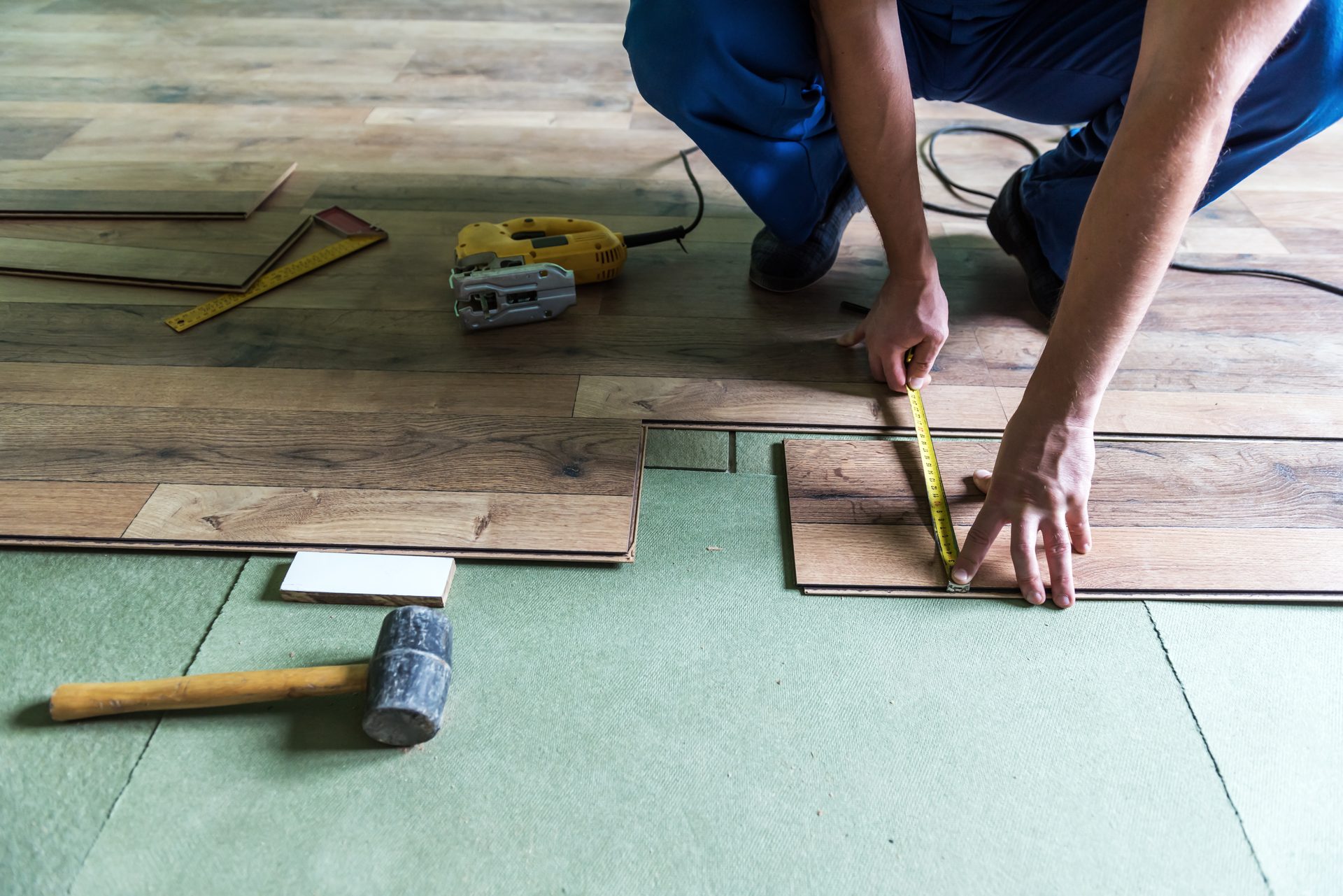 Handwerker verlegt neuen Laminatboden inklusive Untergrundvorbereitung