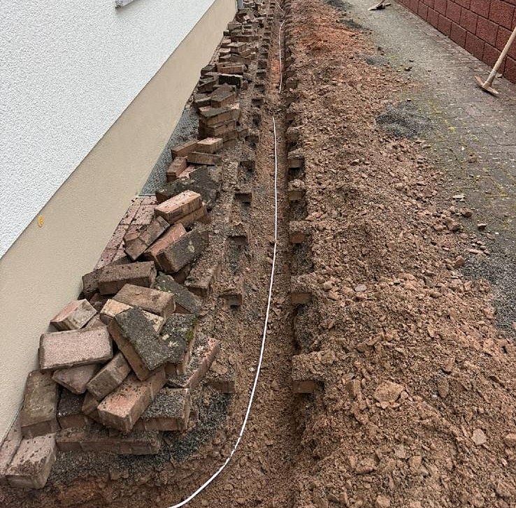 Verlegung des Glasfaser-Mikrorohrs im Leitungsgraben entlang der Hauswand